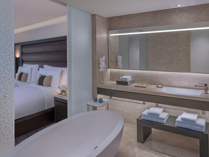 Modern hotelkamer met vrijstaand bad, grote spiegel en uitzicht op het bed.