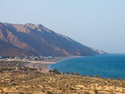 Coastline with blue sea, sandy beach, and mountains in the background under clear sky.