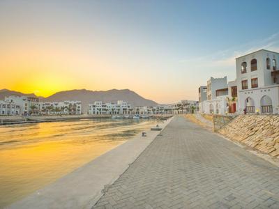 Waterfront promenade with white buildings and mountains in the background at sunset