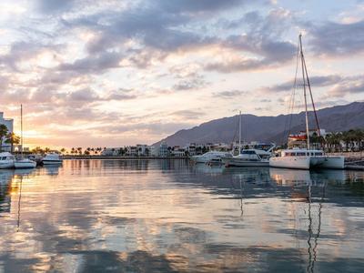 Harbor with yachts and mountains in the background at sunset with clouds in the sky.