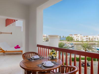 Balcony with wooden table and chairs set with plates, view of palm trees and white buildings under blue sky.