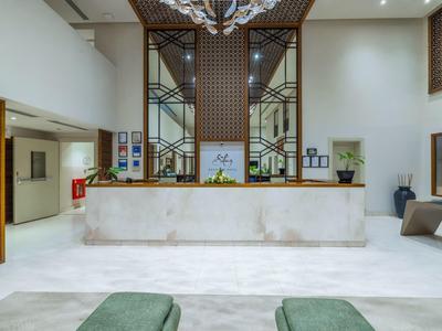 Bright hotel lobby with white marble reception desk and decorative wood and glass walls.