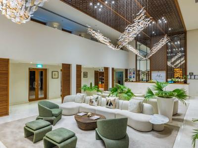 Modern hotel lounge with white seating, green chairs, and hanging art installation in a bright room.