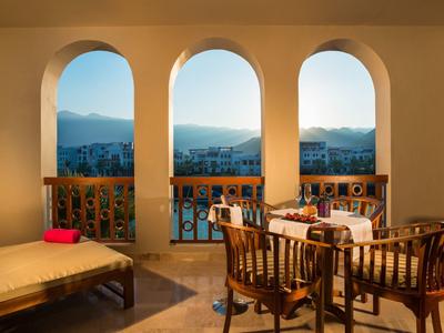 Balcony with three arches, table and chairs overlooking mountains at sunset.