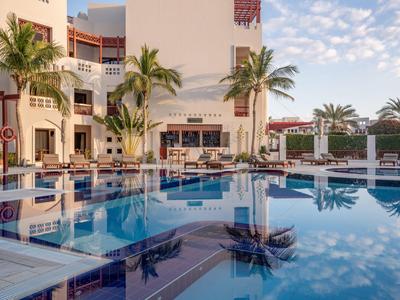 Modern hotel pool with lounge chairs and palm trees at sunrise.