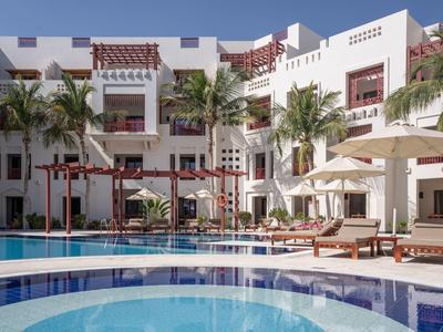Hotel with white building, palm trees, swimming pool, and sun loungers under umbrellas