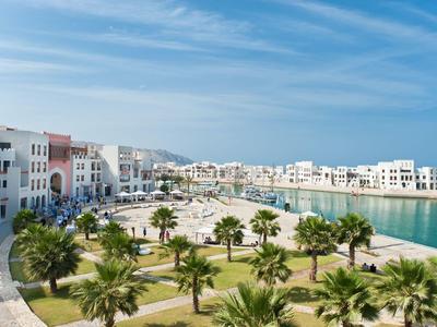 Modern coastal town with white architecture, green palm trees, and clear blue sky.