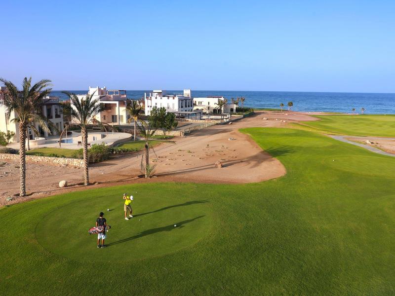 Two golfers on a green golf course overlooking the sea and white buildings in the background.