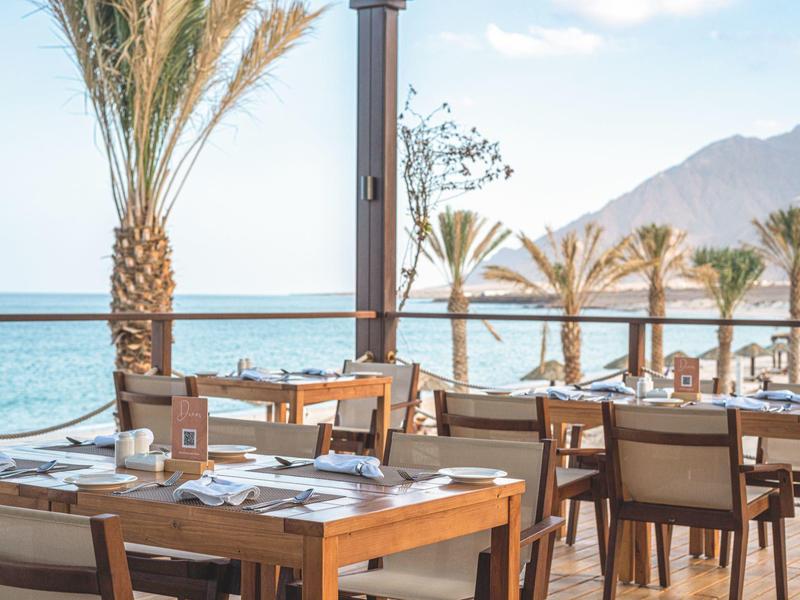Restaurant terrace with wooden tables and palm trees by the sea with mountains