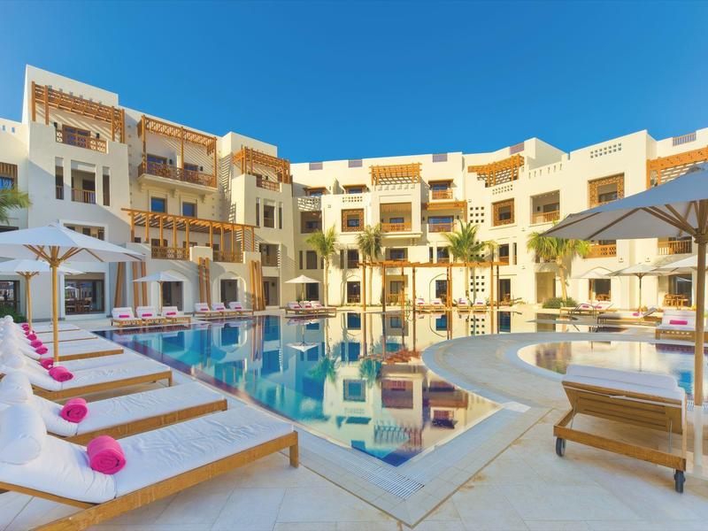 Modern hotel pool with lounge chairs and white umbrellas in daylight.