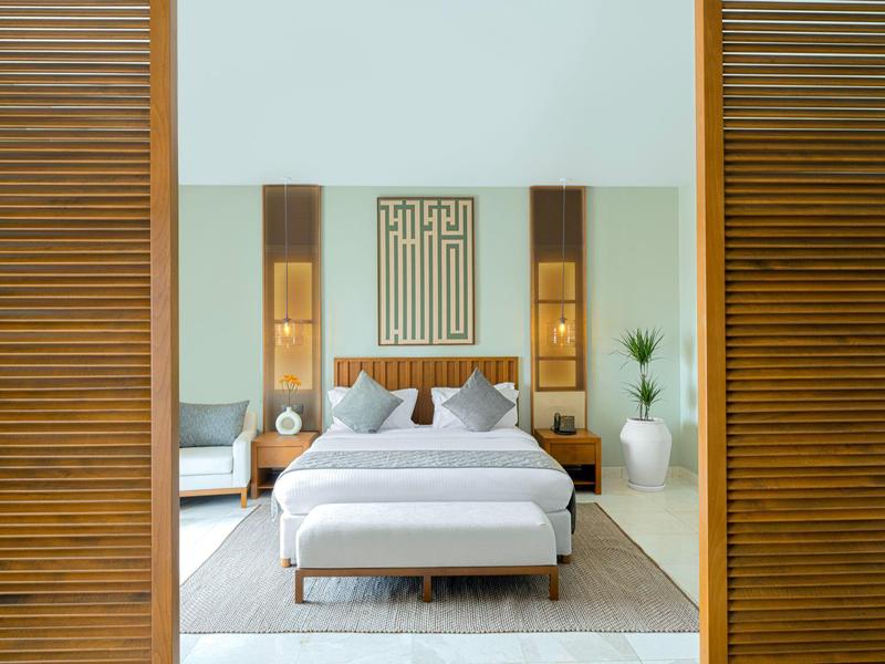 Modern hotel room with large bed, wooden walls, and minimalist decoration.