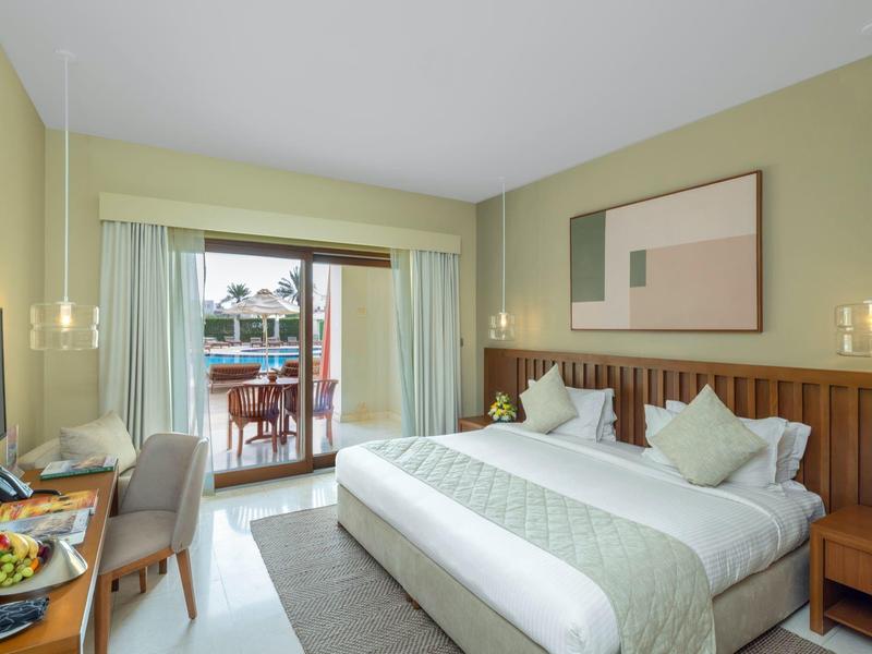 Bright hotel room with king-size bed, balcony, and modern lamps on the headboard wall.