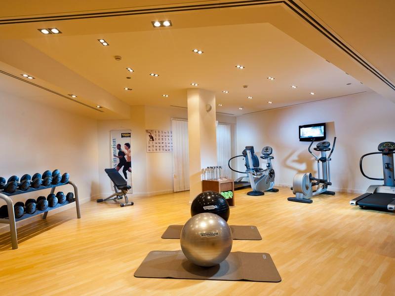 Modern fitness room with dumbbells, exercise balls, and cardio machines in a bright space.