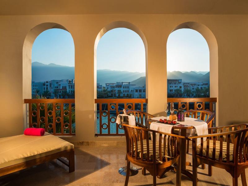 Balcony with three arches, table and chairs overlooking mountains at sunset.