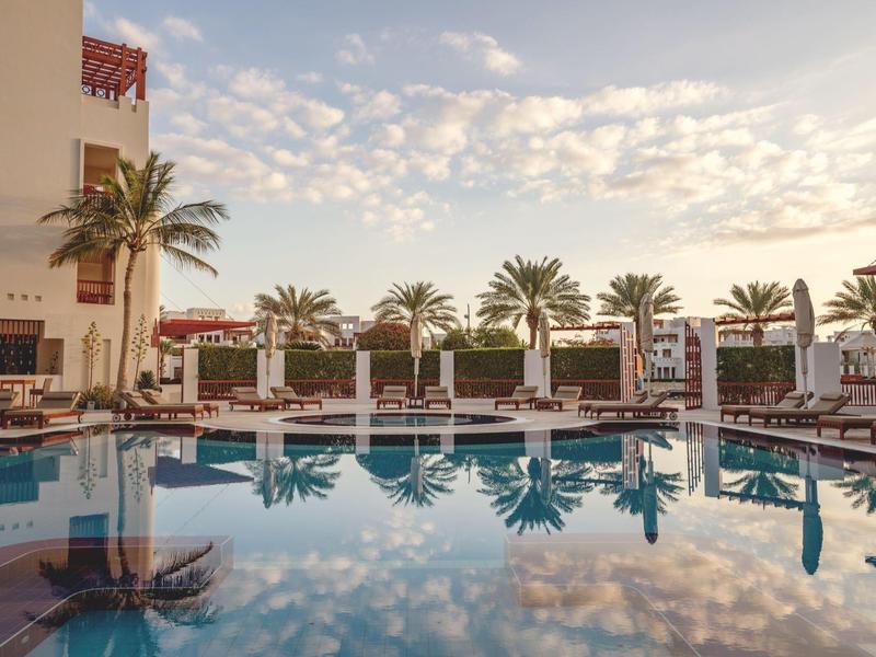 Calm pool with sun loungers and palm trees under a cloudy sky