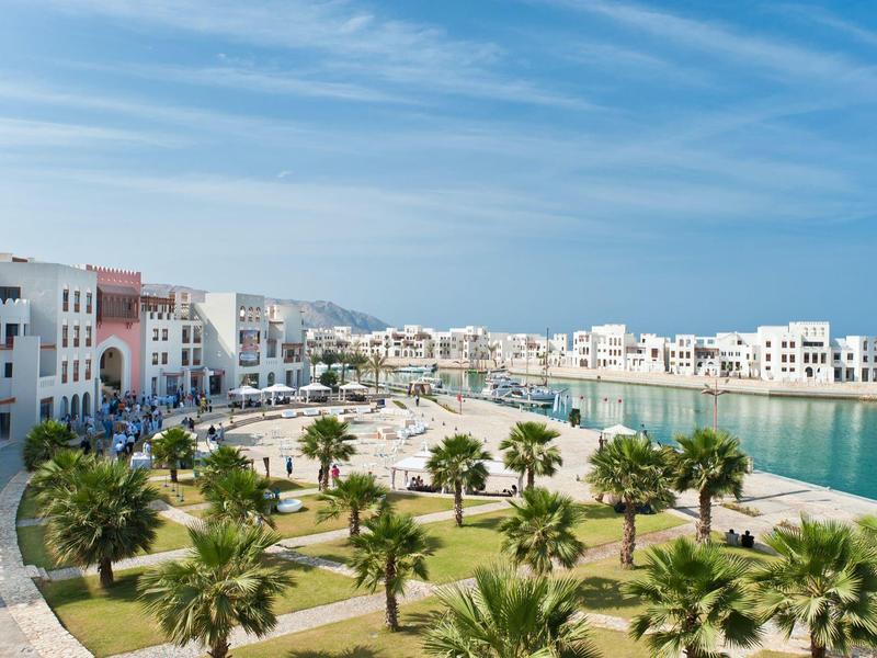 Modern coastal town with white architecture, green palm trees, and clear blue sky.