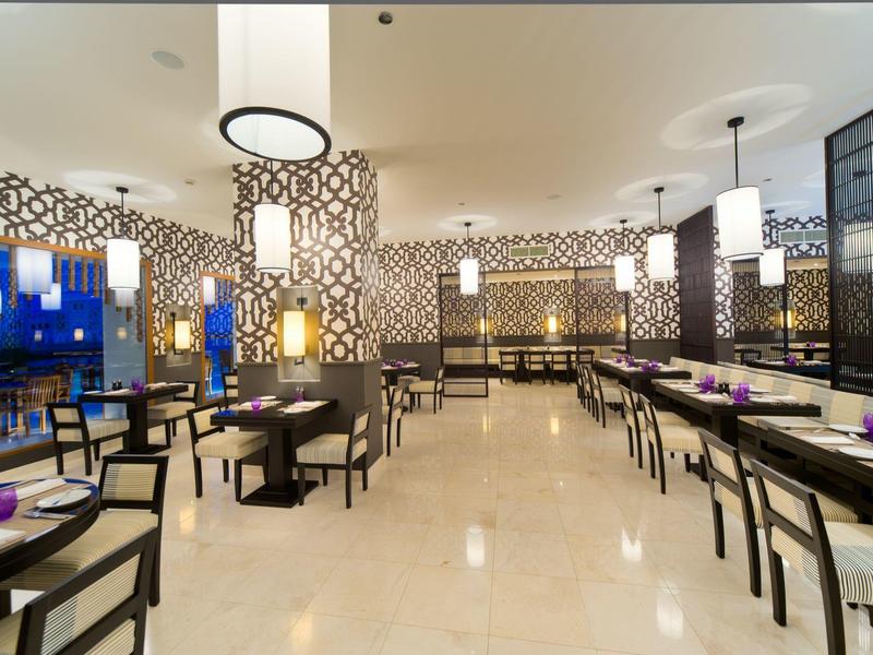 Modern hotel restaurant interior with benches, chairs, and decorative wall lights.