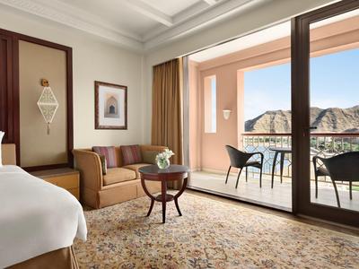 Jasný hotelový pokoj s pohovkou, malým stolem a balkonem s výhledem na hory.