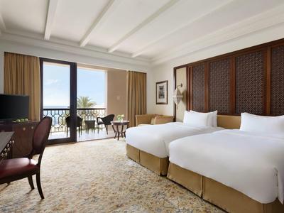 Světly hotelový pokoj se dvěma jednolůžky, balkonem a výhledem na moře.