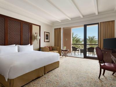 Světý hotelový pokoj s velkou postelí a balkonem s výhledem na palmy.