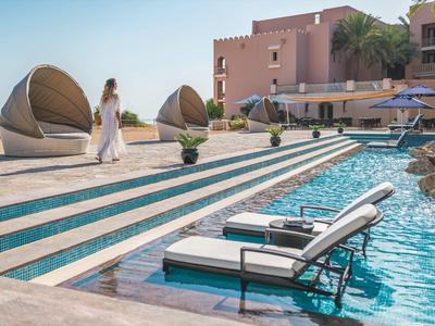 Lounge nábytek a lehátka u hotelového bazénu s palmami a slunečníky.