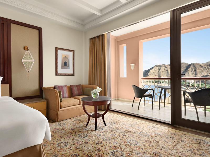 Jasný hotelový pokoj s pohovkou, malým stolem a balkonem s výhledem na hory.