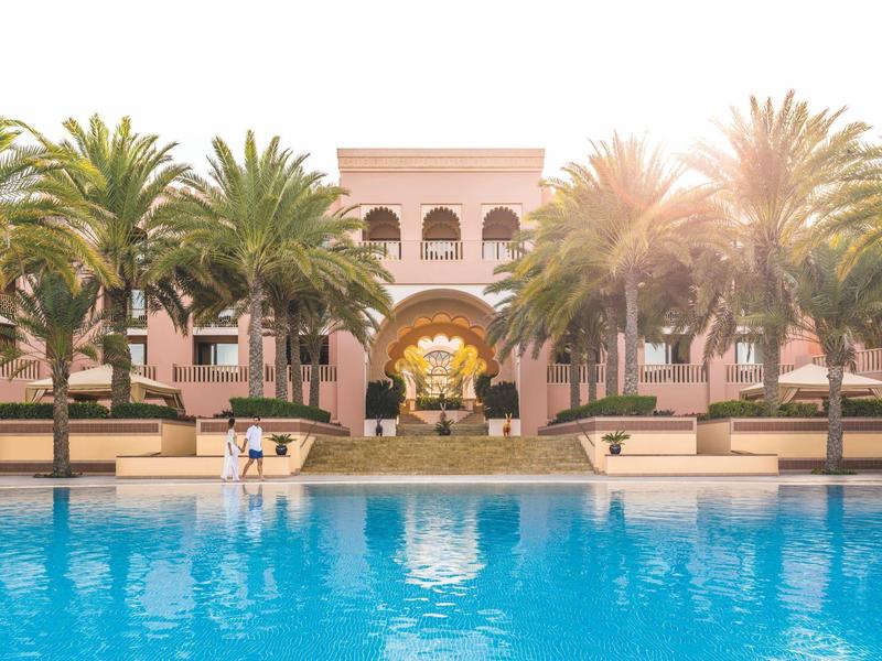 Hotel s palmami a velkým bazénem na slunečním světle v pozadí