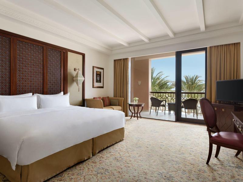 Světý hotelový pokoj s velkou postelí a balkonem s výhledem na palmy.