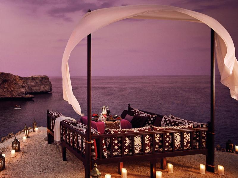 Romantická posezení s polštáři a svíčkami u moře při západu slunce.