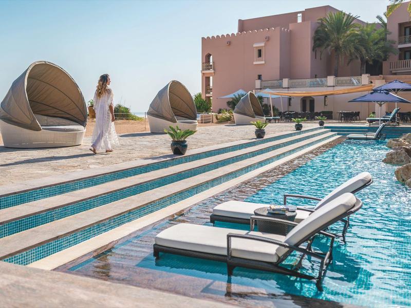 Lounge nábytek a lehátka u hotelového bazénu s palmami a slunečníky.