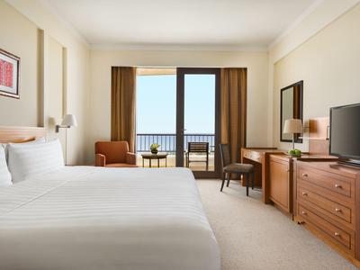 Chambre d'hôtel moderne avec lit double, télévision, coin salon et balcon avec vue sur la mer.