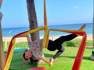 Person macht Yoga-Pose an rot-gelbem Tuch im Freien mit Meerblick.