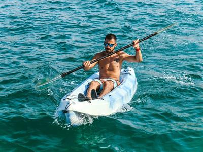 Mann paddelt in weißem Kajak auf blauem, leicht welligem Wasser bei Sonnenschein.