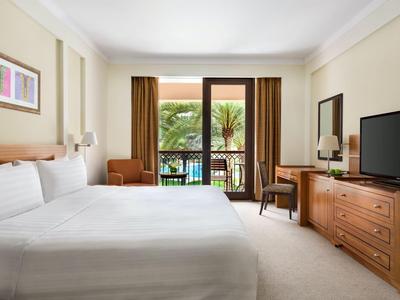 Chambre d'hôtel lumineuse avec lit double, télévision, bureau et balcon avec vue sur des palmiers.