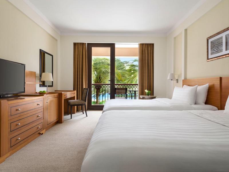 Chambre d'hôtel avec deux lits, balcon et vue sur des palmiers.