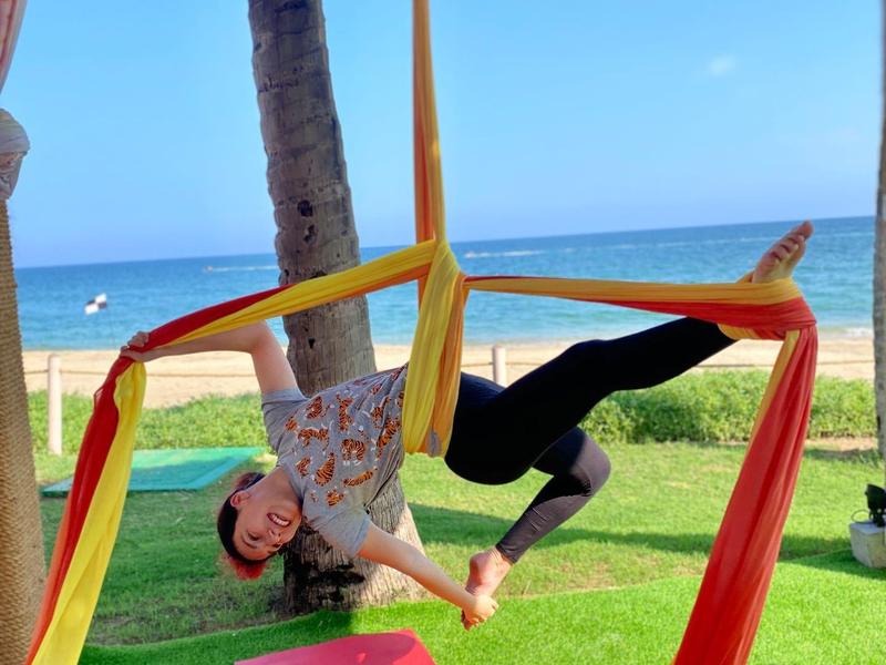 Personne pratiquant le yoga aérien en plein air avec un tissu rouge et un ciel bleu en arrière-plan.