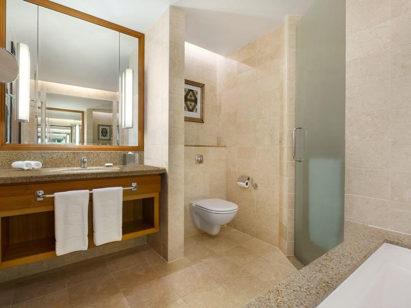 Salle de bain moderne avec carrelage clair, WC suspendu, grand miroir et meubles en bois.