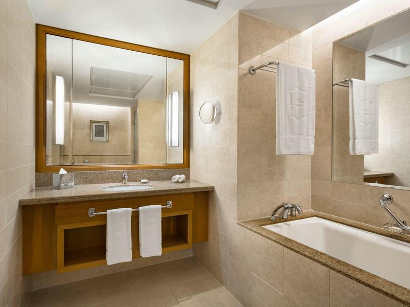 Salle de bain moderne avec baignoire, lavabo et grands miroirs aux tons neutres.