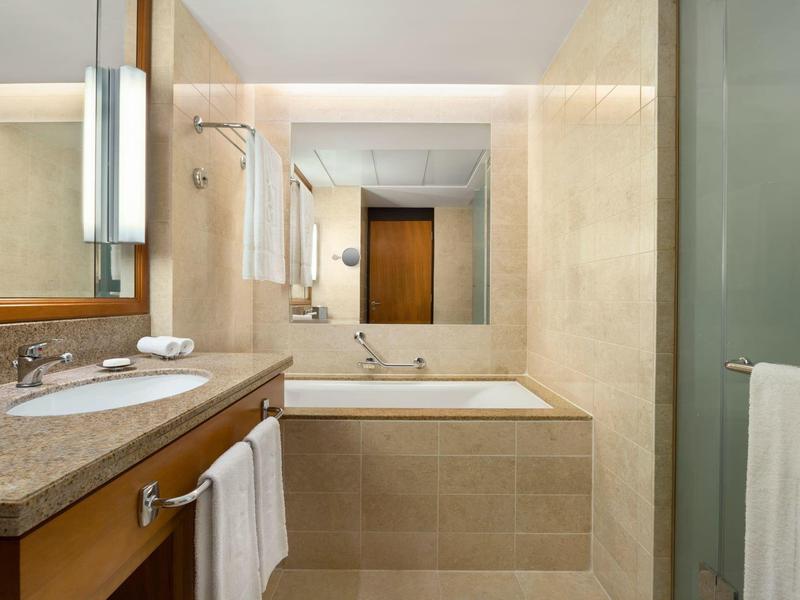 Salle de bains moderne avec baignoire, lavabo et grands miroirs aux couleurs neutres.