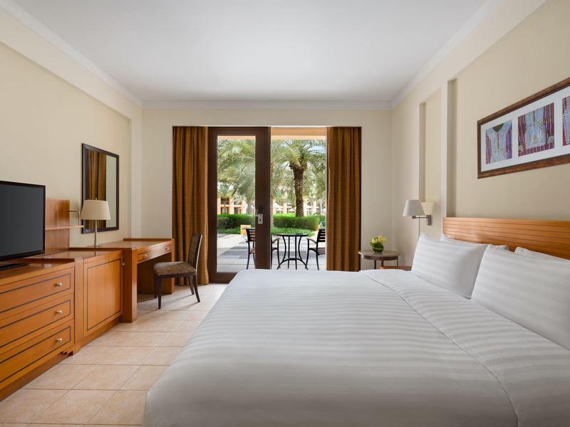 Chambre d'hôtel lumineuse avec grand lit, TV, commode et balcon donnant sur le jardin.