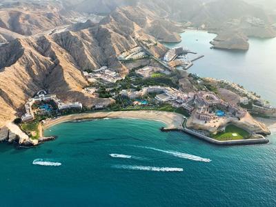 Aerial view of a coastal bay with beach, hotels, and mountains in the background.