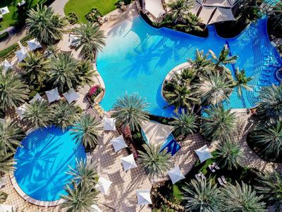 Aerial view of a luxury hotel pool area with palm trees and multiple pools.