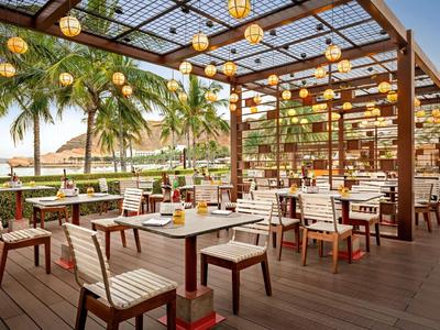 Open-air restaurant with wooden furniture and hanging lights by the beach.