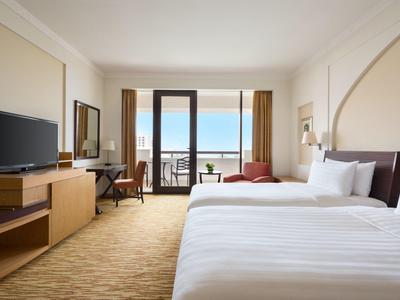 Modern hotel room with large bed, desk, and sea view from the balcony.
