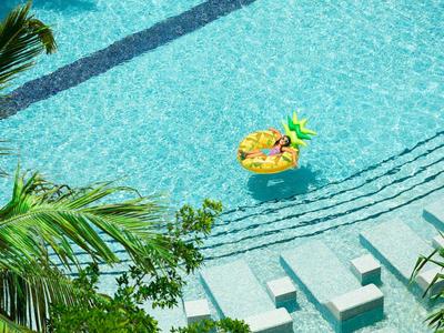 Blue pool with steps and inflatable yellow flamingo, surrounded by green plants.