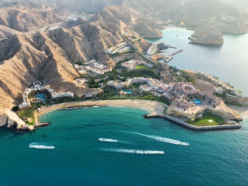 Aerial view of a coastal bay with beach, hotels, and mountains in the background.
