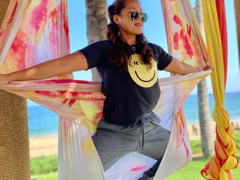 Woman sitting relaxed in hanging chair overlooking the sea, wearing sunglasses.
