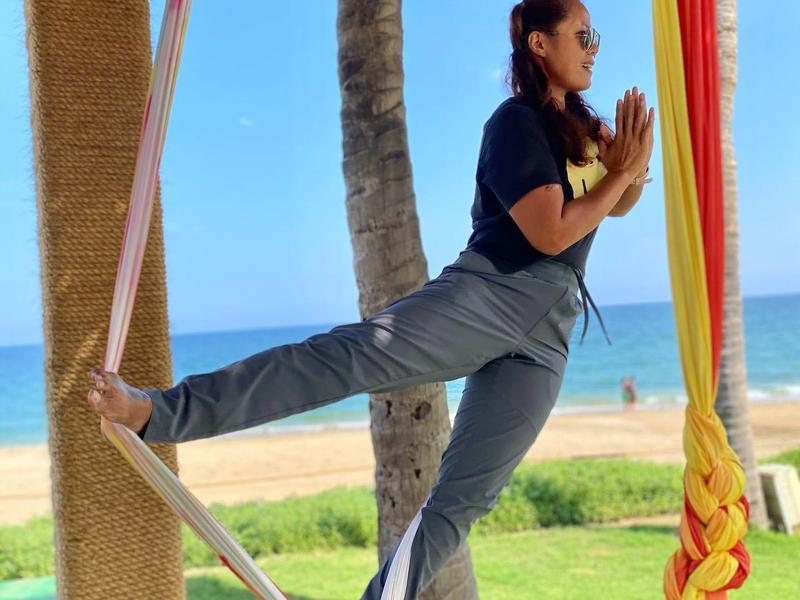 Person practicing yoga in a hammock by the beach with ocean view.