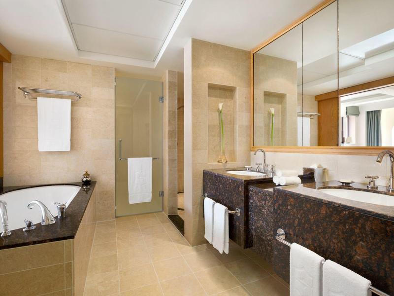Modern bathroom with double sinks, bathtub, and separate shower in warm tones.