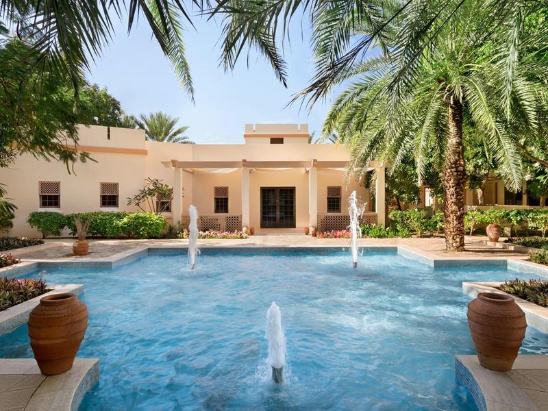 Luxurious hotel with large pool, fountains and palm trees in sunny garden.